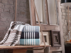 Soft white bath towel from SaaSoh Mykonos Collection with blue and beige geometric patterns, displayed on a wooden rack.